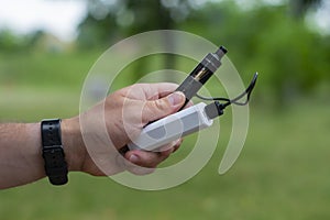 A man holds a power bank in his hands and charges an electronic cigarette against the backdrop of nature