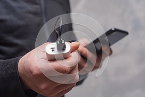 Man holds a power bank in his hands and charges a smartphone against a concrete wall