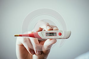 Man holds a red fever thermometer with high temperature in his hand