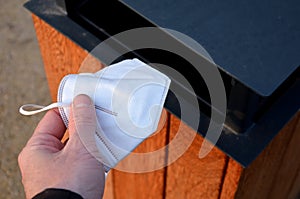 Man holds a respirator in his hand and is about to throw it in the trash in the park. he picked up the respirator on the ground to