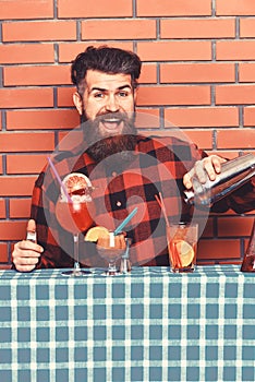 Man holds shaker on brick wall background. Barman with beard and happy face makes cocktail. Barman or hipster makes