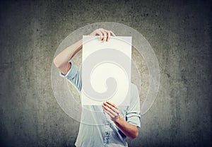 A man holds a sheet of white paper in front of his face