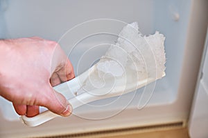 A man holds a shovel with ice on the background of a freezer. Defrosting the freezer.