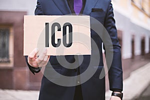 The man holds a sign in his hand with the inscription `ICO` Initial Coin Offerering. Digital Electronic Trade Market Stock Ind