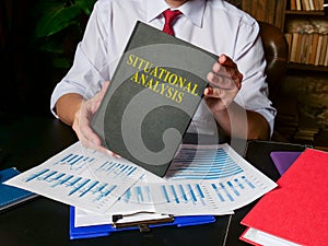 Man holds situational analysis report and pile of charts.