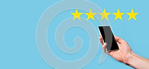 Man holds smart phone in hands and gives positive rating, icon five star symbol to increase rating of company concept on blue