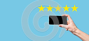 Man holds smart phone in hands and gives positive rating, icon five star symbol to increase rating of company concept on blue