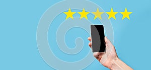 Man holds smart phone in hands and gives positive rating, icon five star symbol to increase rating of company concept on blue