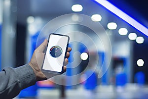 A man holds a smartphone with a digital fuel meter on the screen against the background of a night gas station for a car