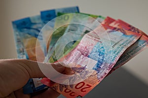 Man holds swiss banknotes in his hand and counts his monthly income.