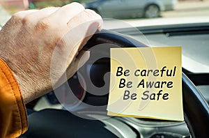A man holds on to the steering wheel, next to a sticker with the inscription - Be careful. Be aware. Be safe.