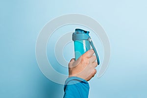 A man holds a water bottle high in his hand on a blue background. Sport drink concept. Copy space for your text