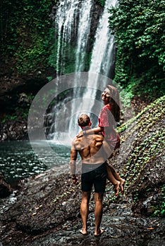 A man holds a woman in his arms at the waterfall. Couple at the waterfall, rear view. Honeymoon trip.