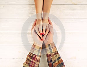 Man holds woman`s hands top view image on white wooden backdrop. Couple in love consept.