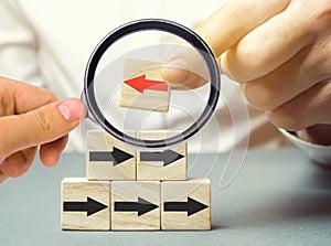 A man holds a wooden block with red arrow facing the opposite direction black arrows. Individual opinion. Stand out from the crowd