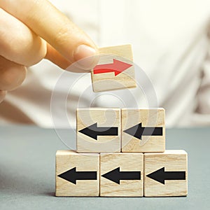 A man holds a wooden block with red arrow facing the opposite direction black arrows. Individual opinion. Stand out from the crowd