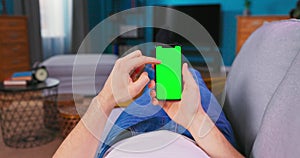 Man at Home Lying on a Couch using Smartphone with Green Mock-up Screen, Doing Swiping,