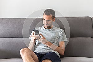 Man at home sitting on couch reading phone message