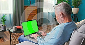 Man at Home Sitting on a Couch Working on Green Mock-up Screen Laptop Computer. Guy