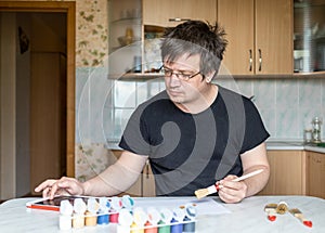 A man at home at the table. in one hand he holds a brush. the other is checked in the tablet.