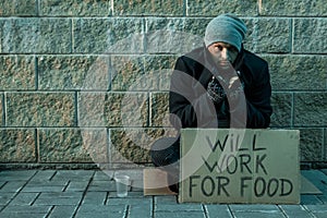 A man, homeless, a man asks for alms on the street with a sign will work for food. Concept of homeless person, addict, poverty,