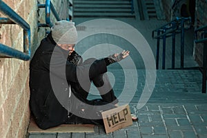 A man, homeless, a person asks for alms on the street with a Help sign. Concept of homeless person, addict, poverty, despair