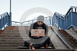 A man, homeless, a person asks for alms on the street with a Help sign. Concept of homeless person, addict, poverty, despair