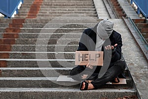 A man, homeless, a person asks for alms on the street with a Help sign. Concept of homeless person, addict, poverty, despair