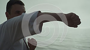 Man honing fighting skills training punches standing beach at sunrise close up.