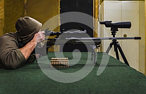 A man in a hood reload and shoots with a sniper rifle at a shooting range