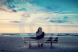 Man in hood sitting on a lonely bench on the beach
