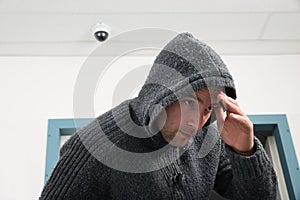 Man In Hooded Sweatshirt With Cctv Camera Behind photo