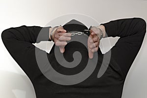 A man in a hooded sweatshirt holds his hands above his head while handcuffed in police handcuffs.