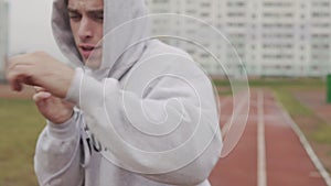 Man in hoodie boxing with invisible opponent at stadium. Young man training