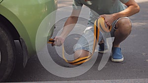 A man hooking a tow rope to a green passenger car.