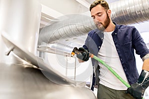 Man with hose working at craft beer brewery kettle