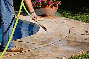 Man hosing pool paving, Spain.