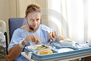 Man in hospital room eating healthy diet clinic food in upset moody face expression