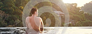 Man in hotel outdoor swimming pool looking at pictorial tropical forestry hilly landscape