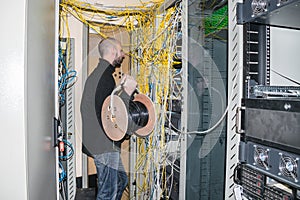 Man with a hub of utp cable works in the server room of the data center. The technician is near the racks with the servers. The