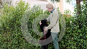 Man hugging his black dog next to a bush full of leaves