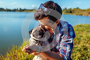 Man hugging and playing with pug dog in park. Man walking with pet by spring lake. Friends enjoying nature