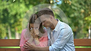 Man hugging and supporting crying wife in park, relative death, togetherness