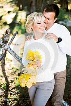 Man hugs woman from behind with a bouquet of yellow leaves in her hands