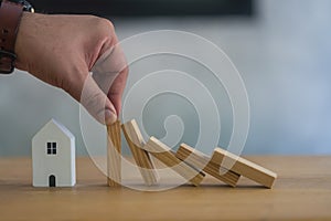 Man human hand stopping the wooden blocks from falling on house model. Real estate house insurance