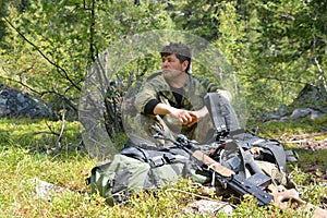 Man, hunter, sitting near the rifle and backpack in the taiga.