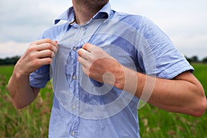 Man with hyperhidrosis sweating very badly under armpit in blue shirt, on grey photo