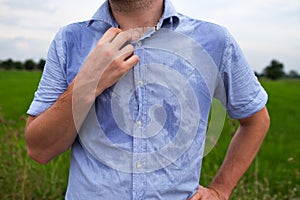 Man with hyperhidrosis sweating very badly under armpit in blue shirt, on grey photo