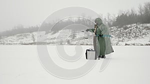 Man with ice drill in hands on frozen ice lake in winter. Portrait of fisherman drilling ice hole on ice pond. Winter fishing