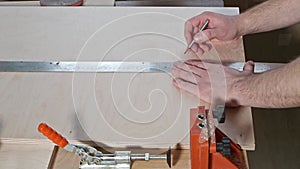 Man in independent manufacture of furniture at home using metal ruler measures the desired distance on sheet of plywood